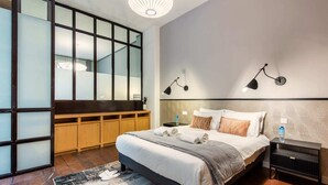 A modern hotel room with a large bed, a wooden bench, and a view through a frosted glass partition. - Sweett | Artois - Three Bedroom Apartment, Sleeps 6 (Paris)