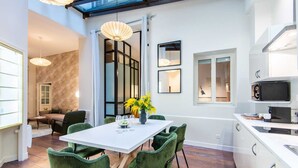 A modern kitchen with a white countertop, green upholstered chairs, and a dining table with a vase of yellow flowers. - Sweett | Artois - Three Bedroom Apartment, Sleeps 6 (Paris)