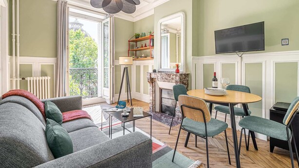 Una sala de estar con sofá, mesa de comedor con sillas, chimenea y televisor montado en la pared.