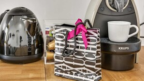 A coffee maker, a gift bag, and a mug on a wooden table.