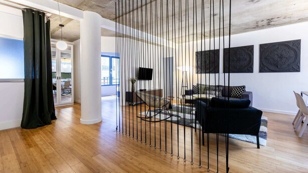 A modern living room with a black sofa, a coffee table, and a TV mounted on the wall. There are three large black decorative panels on the wall. - Sweett | Milan I - Two Bedroom Apartment, Sleeps 6 (Paris)