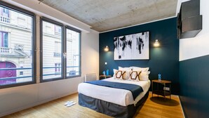 A modern bedroom with a large bed, a view of the city through large windows, a painting on the wall, and a small bedside table with a water bottle. - Sweett | Milan I - Two Bedroom Apartment, Sleeps 6 (Paris)