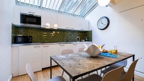 A modern kitchen with white cabinets, a microwave, and a green backsplash. There's a dining table with chairs and a clock on the wall. - Sweett | Milan I - Two Bedroom Apartment, Sleeps 6 (Paris)
