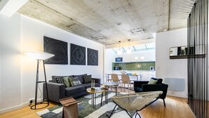 A modern living room with a sofa, coffee table, and a dining area with chairs. There is a kitchen visible through an open door. - Sweett | Milan I - Two Bedroom Apartment, Sleeps 6 (Paris)