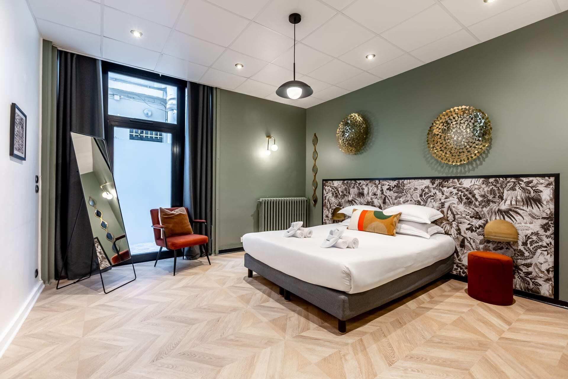 Ett modernt hotellrum med en stor säng, en röd fåtölj, en spegel och utsikt över omgivningarna.