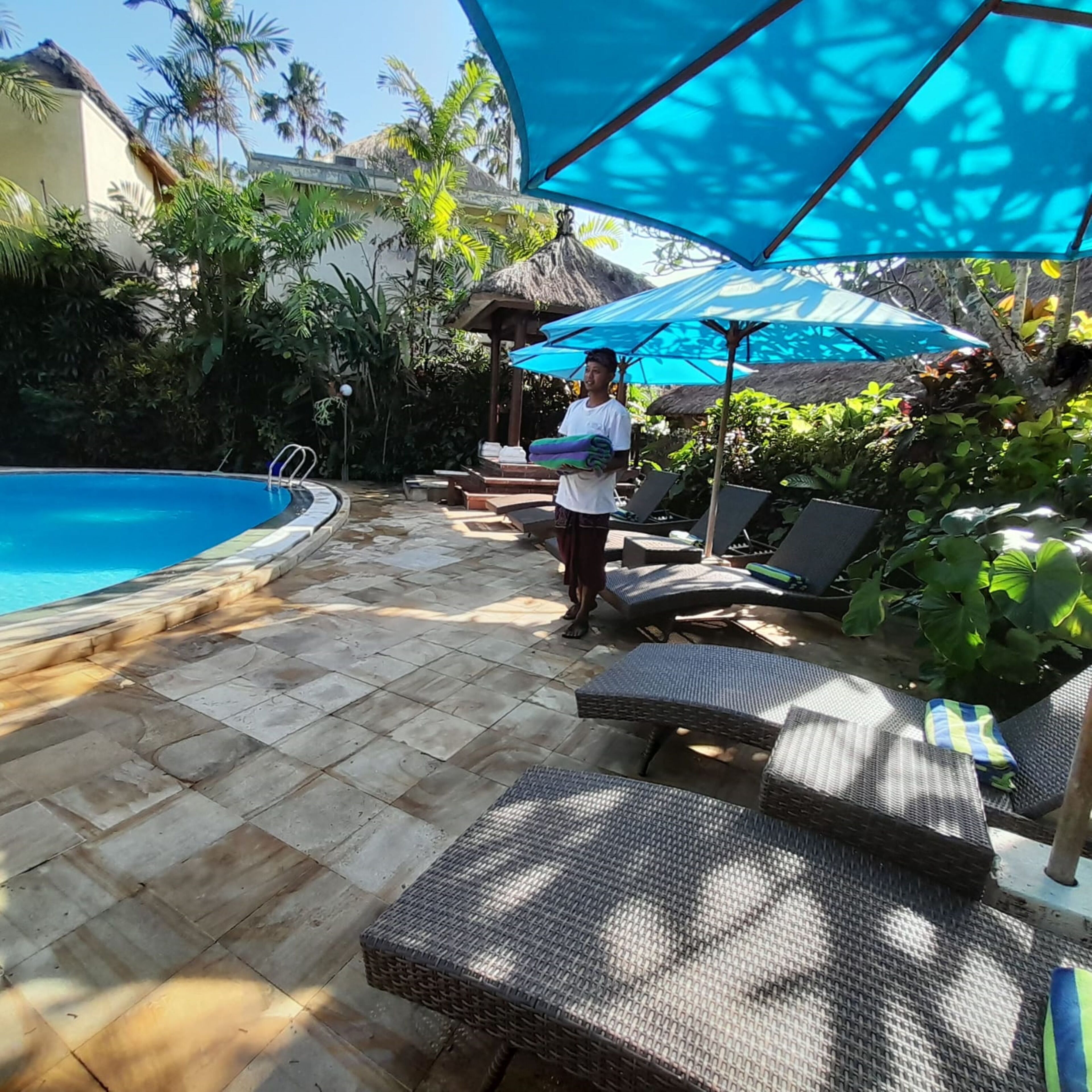 A poolside area with lounge chairs, umbrellas, and a person standing near the pool.