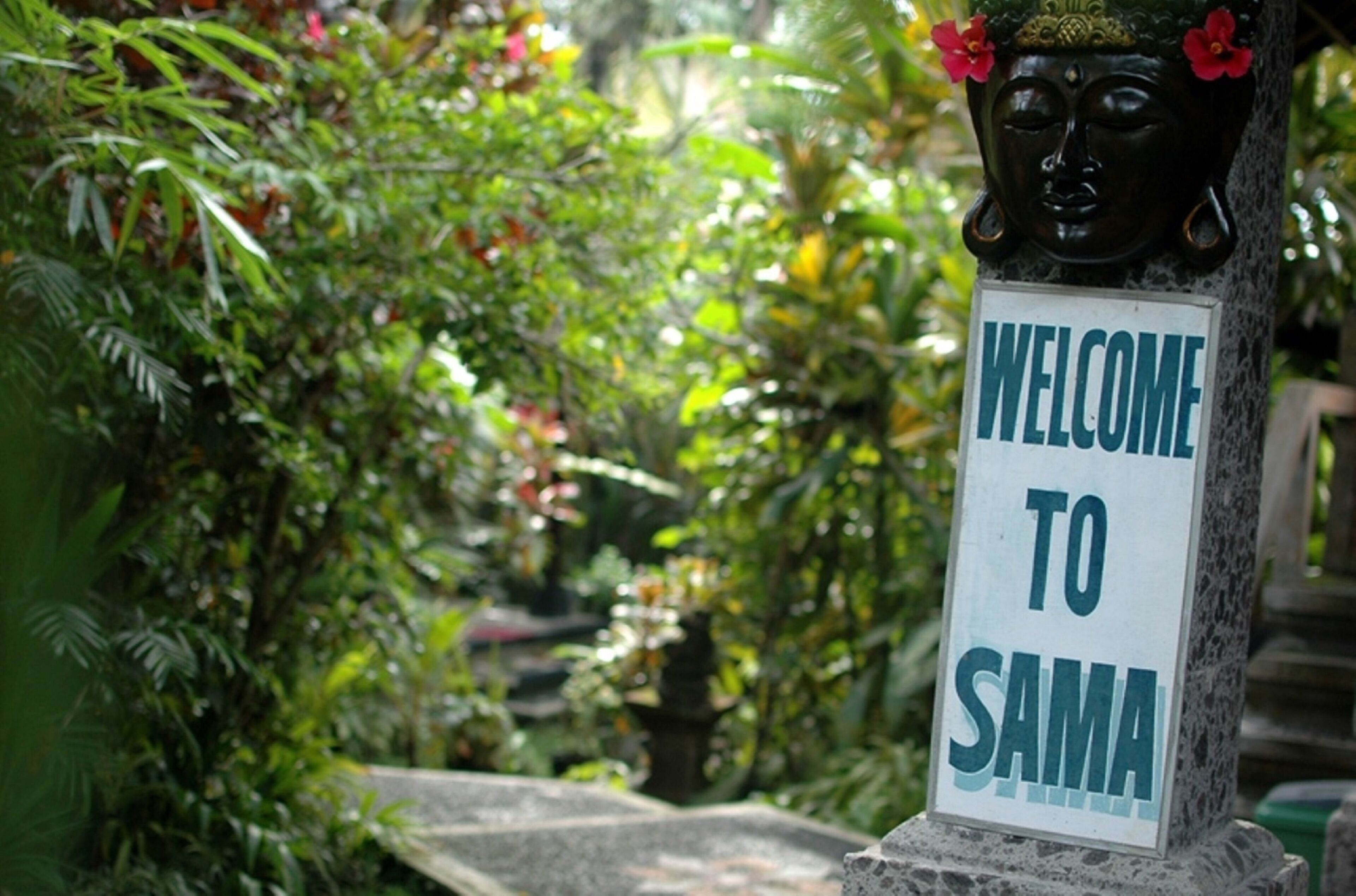 A welcome sign to SAMA with a Buddha statue and lush greenery in the background.