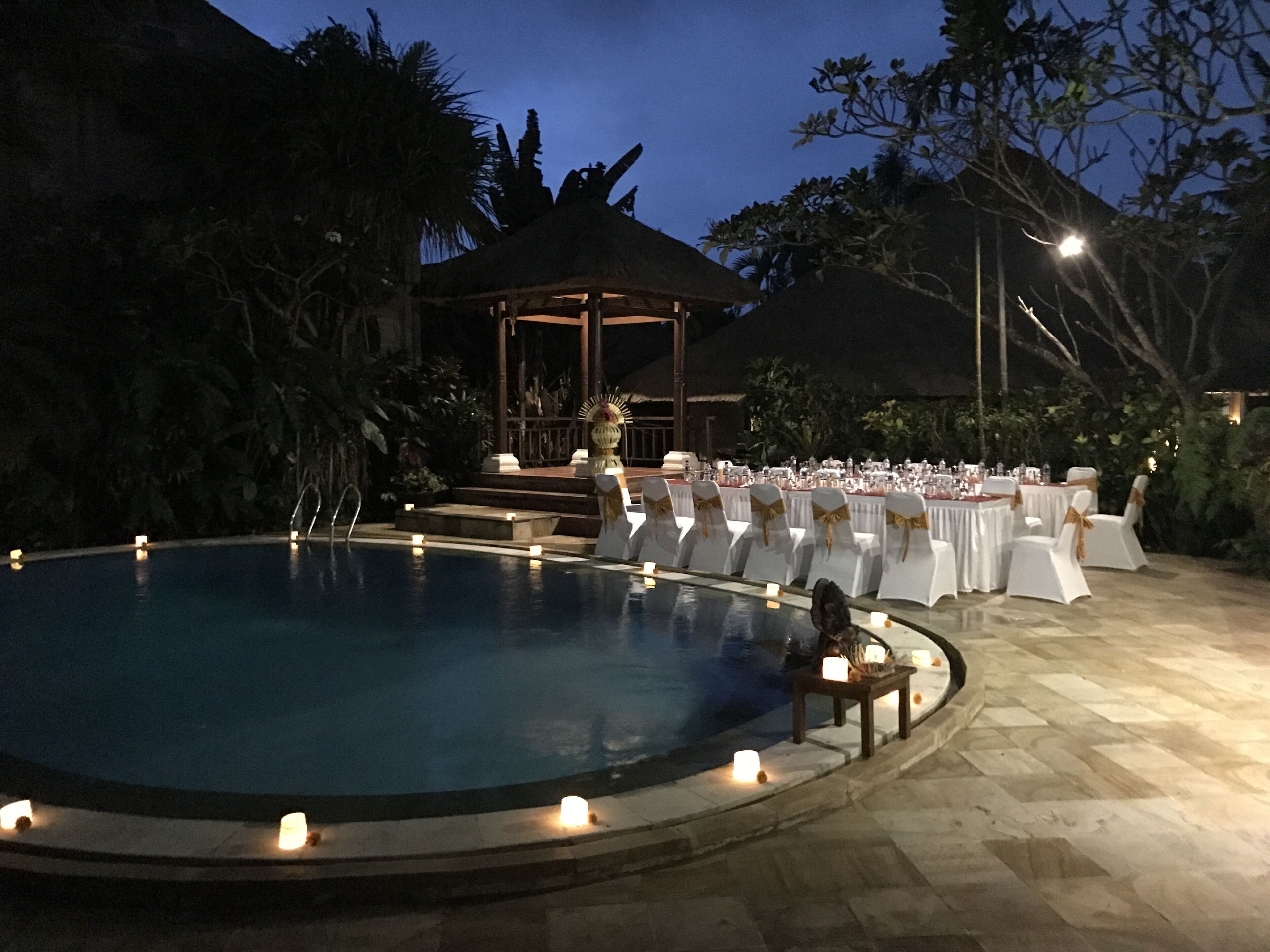 A poolside setting with a covered seating area, tables set for dining, and a gazebo in the background.