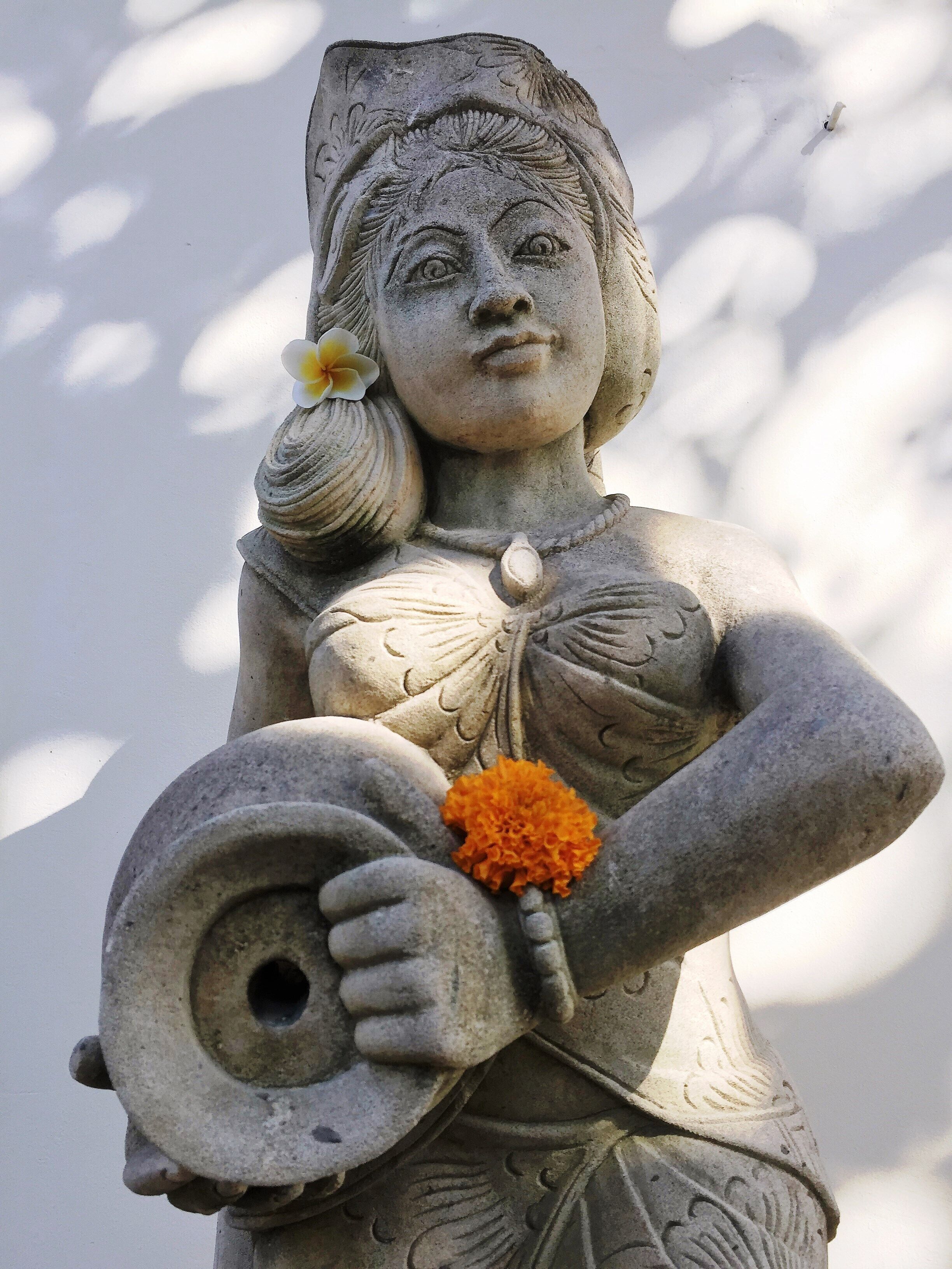 A stone statue of a woman holding a circular object and a flower.
