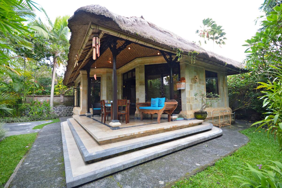 A thatched-roof structure with a porch, outdoor seating, and a garden.