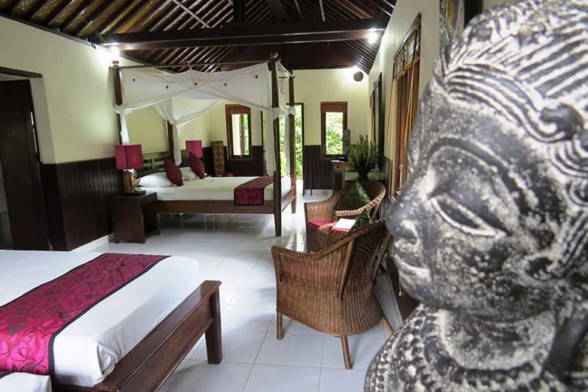 A bedroom with a four-poster bed, a desk with a chair, and a large statue.