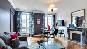 A modern living room with a sofa, a dining table with chairs, a fireplace, and a TV mounted on the wall. - Sweett | Rivoli II - Three Bedroom Apartment, Sleeps 6 (Paris)