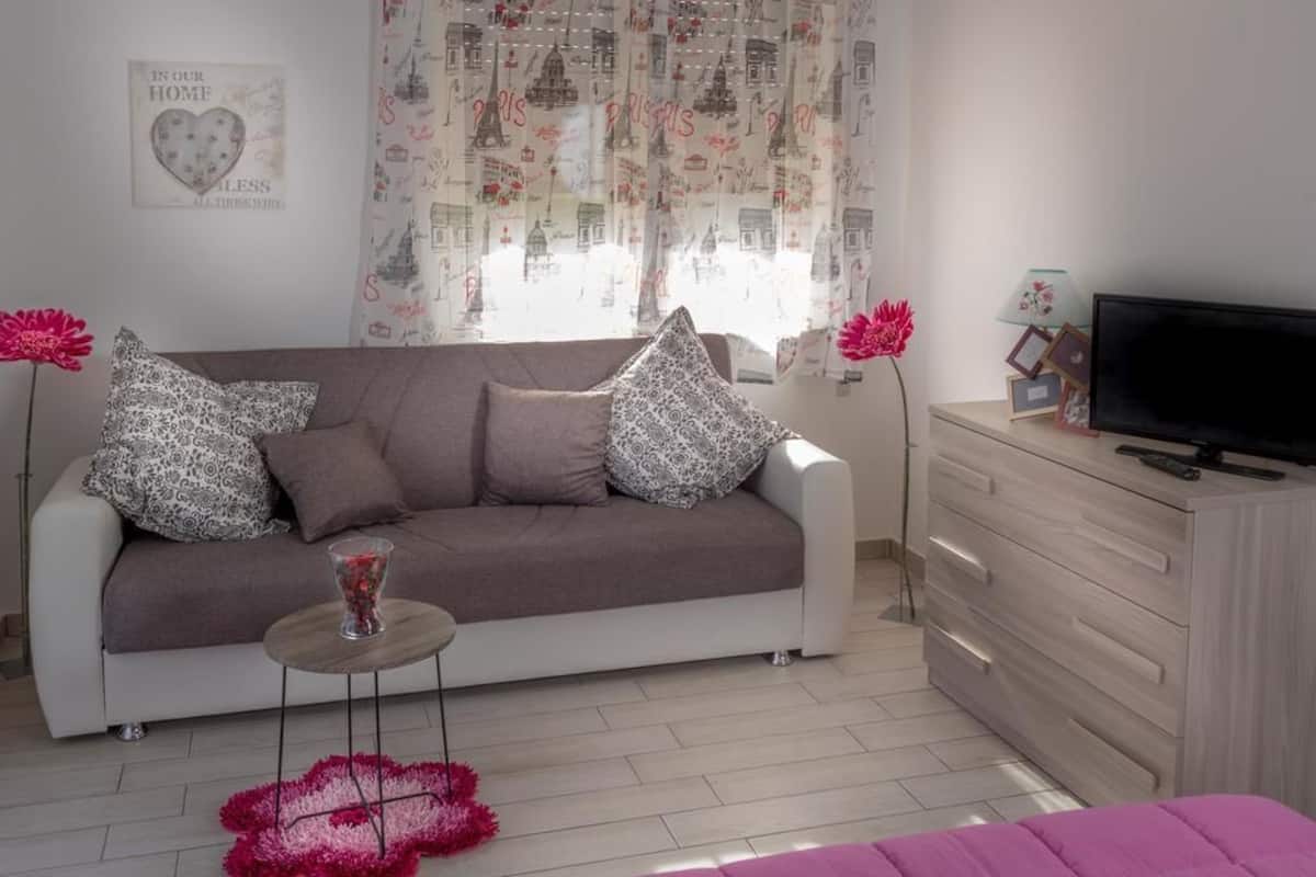 A modern living room with a sofa, decorative pillows, a glass table, and a television.