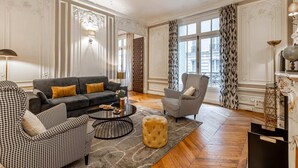 A spacious living room with a grey sofa, houndstooth armchairs, a round coffee table, and a patterned rug.