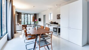 A modern kitchen with white cabinets, a dining area with a wooden table and metal chairs, and a large window providing a view of the outside. - Sweett | Brune VIII - Three Bedroom Apartment, Sleeps 8 (Paris)