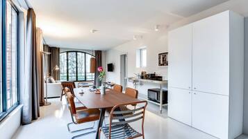 Una cocina moderna con armarios blancos, un comedor con mesa de madera y sillas de metal, y un ventanal que ofrece vistas al exterior.