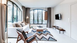 A modern living room with a large window, a sofa, a coffee table, a TV, and a bench. - Sweett | Brune VIII - Three Bedroom Apartment, Sleeps 8 (Paris)