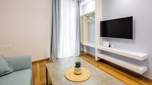 Una sala de estar moderna con un televisor de pantalla plana, un sofá, una mesa de centro con una planta y suelo de madera.