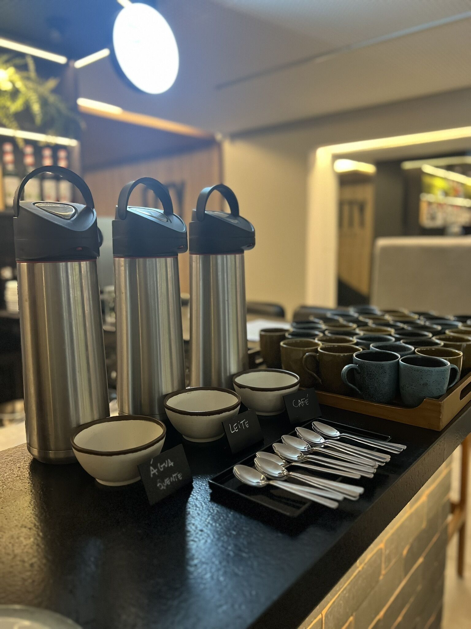 Una estación de café con termos de acero inoxidable, tazas de cerámica y cucharas.