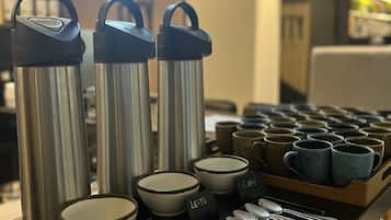 Una estación de café con termos de acero inoxidable, tazas de cerámica y cucharas.