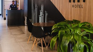 A reception area with a wooden reception desk, a seating area with chairs, and a large potted plant. - Fity Hotel (Recife)