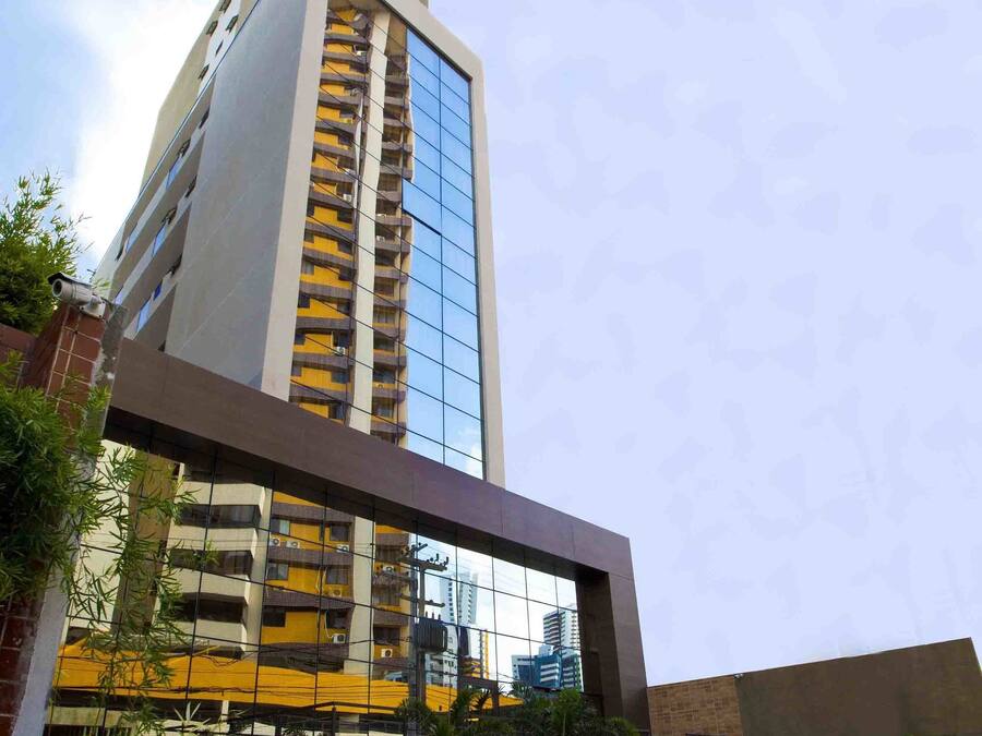 Un moderno edificio de gran altura con fachada de vidrio, terraza en la azotea y un patio ajardinado con plantas.