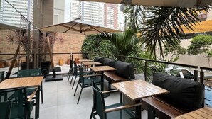 An outdoor cafe with wooden tables and chairs, umbrellas, and a brick wall. - Fity Hotel (Recife)