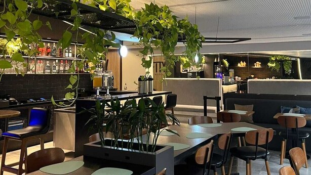 A modern restaurant with a bar area, seating arrangements, and indoor plants. - Fity Hotel (Recife)