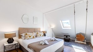 Ein modernes Schlafzimmer mit Bett, Nachttischlampen, einem Hängestuhl und Blick ins Freie.