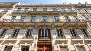 Ein mehrstöckiges Gebäude mit klassischer Architektur, das reich verzierte Balkone und einen zentralen Eingang mit einer Holztür aufweist.