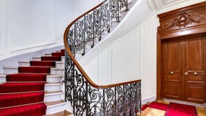Eine prachtvolle Treppe mit aufwendig gestalteten schwarzen Metallgeländern und roten Teppichstufen, die zu einer Holztür führen.