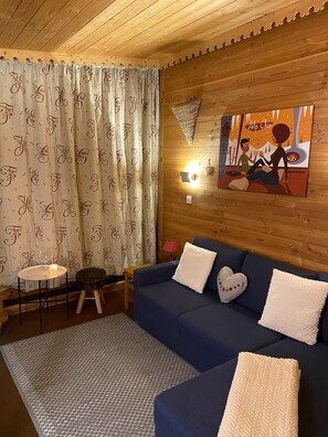 A cozy room with a blue sofa, a small round table, and a wall-mounted lamp.
