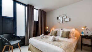 A modern hotel room with a large bed, a chair, a bedside table with a lamp, and a wall-mounted mirror. - Sweett | Brune III - Three Bedroom Apartment, Sleeps 8 (Paris)