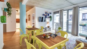 A bright dining area with yellow chairs and a wooden table, a kitchen in the background, and a large window with a view of buildings. - Sweett | Milan IV - Three Bedroom Apartment, Sleeps 8 (Paris)