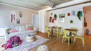 A modern living room with a white sofa, colorful throw blanket, and a dining area with yellow chairs and a wooden table. - Sweett | Milan IV - Three Bedroom Apartment, Sleeps 8 (Paris)