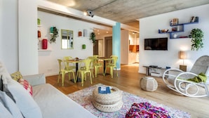 A modern living room with a sofa, a dining area with chairs, a TV, and a hanging plant. - Sweett | Milan IV - Three Bedroom Apartment, Sleeps 8 (Paris)