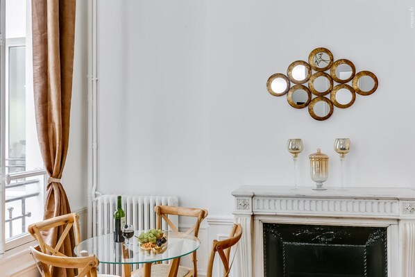 Un comedor con mesa de vidrio, sillas de madera, chimenea y un espejo decorativo en la pared.