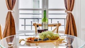 A glass table with a bottle of Merlot wine, grapes, nuts, and blackberries.