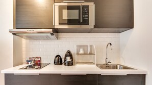 A modern kitchen with a stainless steel microwave, kettle, and coffee maker, a sink with a faucet, and a white tiled backsplash. - Sweett | Saint Germain IV (Paris)