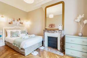 Une chambre à coucher avec un lit, une cheminée, une commode et un grand miroir.