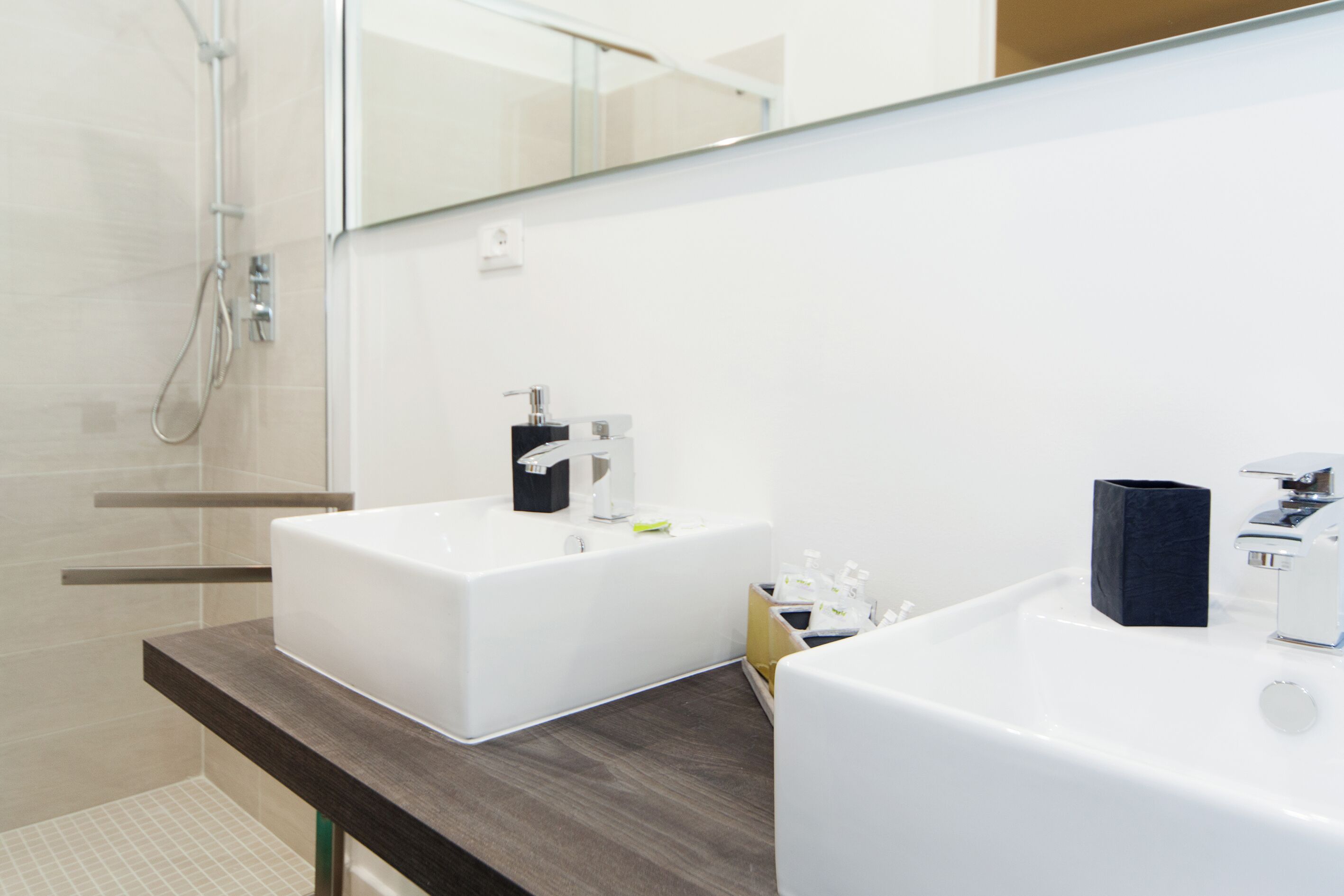 A modern bathroom with two sinks, a shower, and a large mirror.