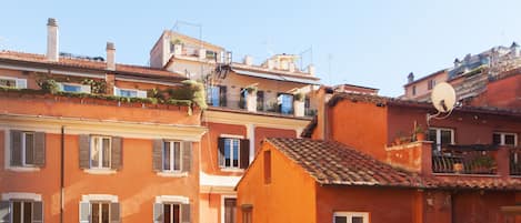 A row of terracotta-colored buildings with uniform window shutters, a satellite dish, and a small balcony with potted plants.