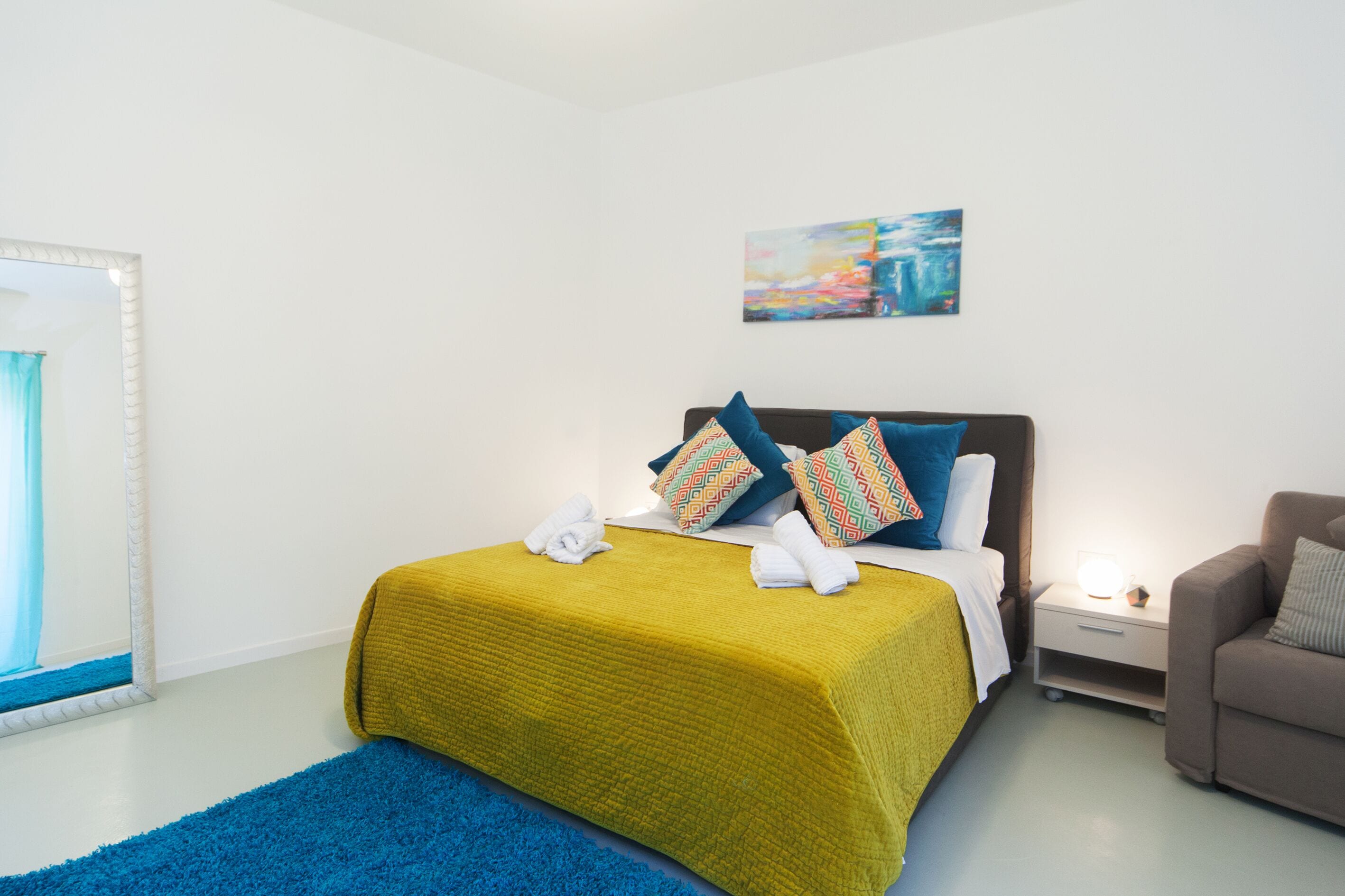 A hotel room with a bed, a nightstand, a chair, and a painting on the wall.