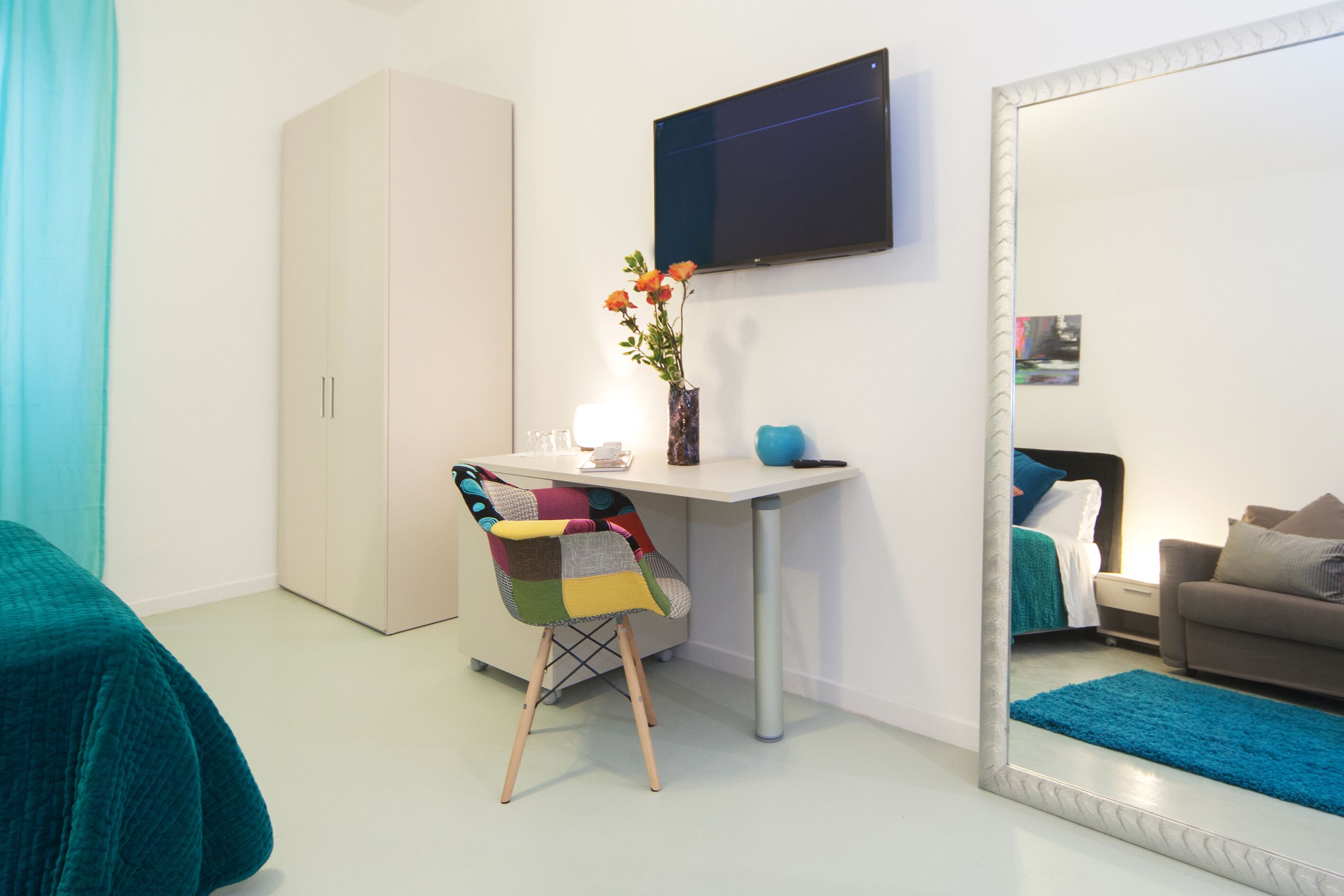 Un dormitorio con cama, escritorio, silla, armario, espejo y televisor.