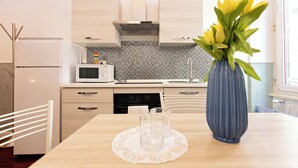 A modern kitchen with light wood cabinets, a microwave, and a sink. There's a vase with yellow flowers on the table. - Casa Bella Pantheon (Rome)