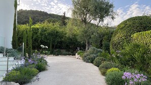 A gravel pathway leading through a garden with various plants and trees. - Panoramic Sea View. Take a walk to the medieval village. (Tourrettes-Sur-Loup)