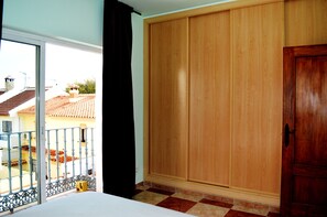 Quarto com um guarda-roupa de madeira grande, varanda com grade de metal e vista para um telhado avermelhado.