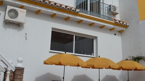 A building with a white facade, yellow trim, and a balcony with a metal railing. There are air conditioning units attached to the building, and a pool area with lounge chairs and yellow umbrellas. - B&B Casa AriGiLi (Fuengirola)