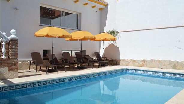 A swimming pool with lounge chairs and yellow umbrellas. - B&B Casa AriGiLi (Fuengirola)
