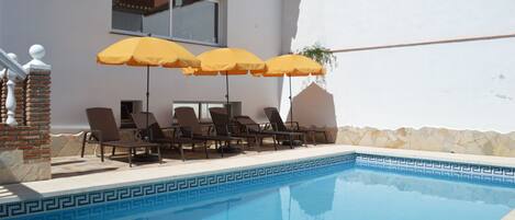 Een buitenzwembad, parasols bij het zwembad en ligstoelen